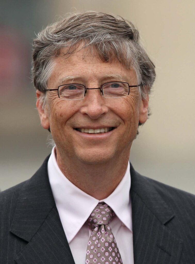 Bill Gates smiling, wearing a black suit, a tie, and sunglasses.