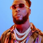 A charismatic portrait of Grammy-winning Nigerian artist Damini Ebunoluwa Ogulu (Burna Boy), showcasing his signature locs, statement jewelry, and a confident expression.