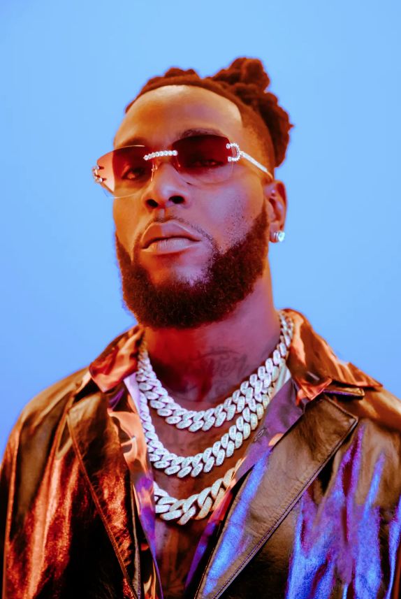 A charismatic portrait of Grammy-winning Nigerian artist Damini Ebunoluwa Ogulu (Burna Boy), showcasing his signature locs, statement jewelry, and a confident expression.