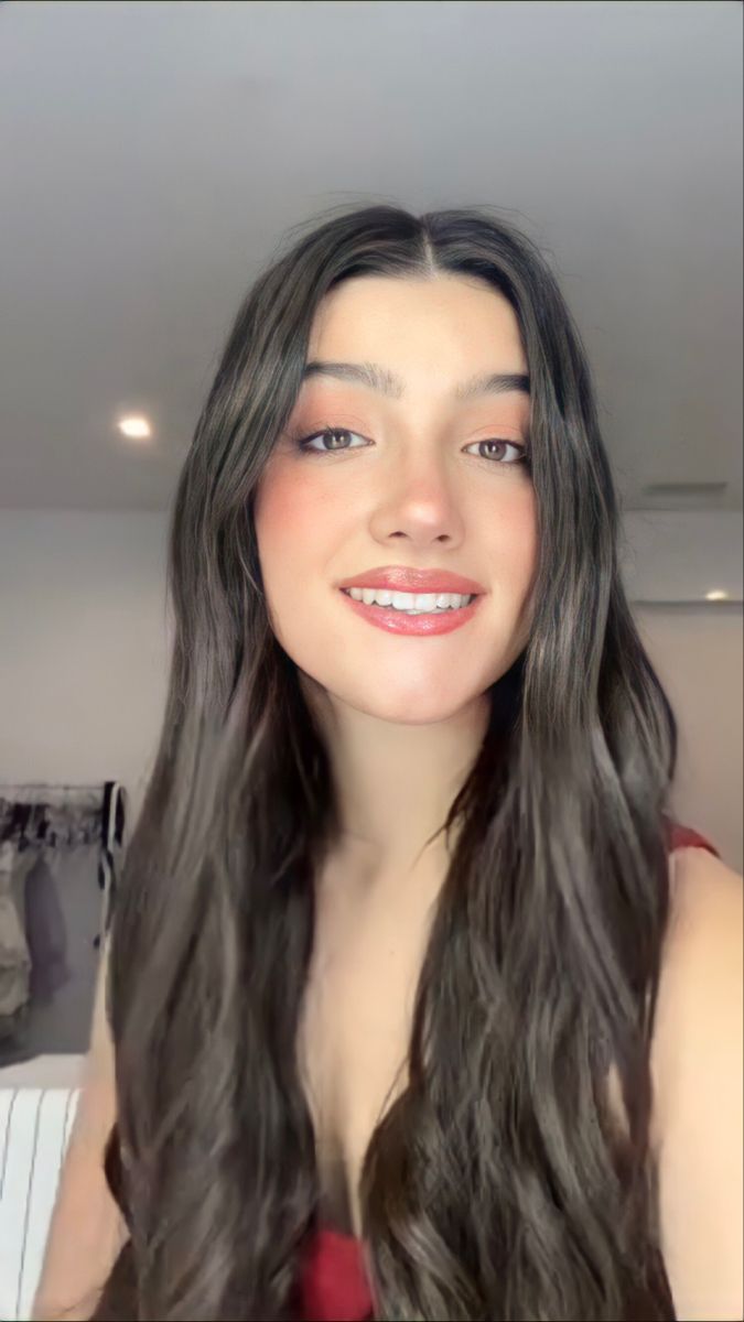 ​A bright, youthful headshot of digital creator Charli D'Amelio, smiling warmly with styled dark hair and natural makeup.
