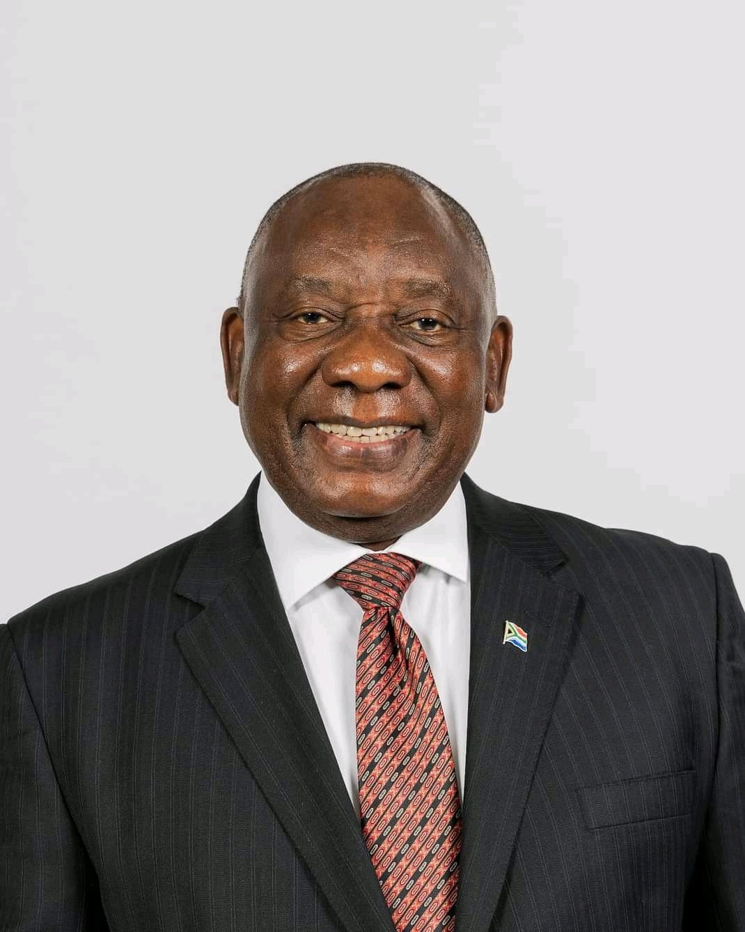 Cyril Ramaphosa, President of South Africa, wearing dark suit and tie and smiling in a neutral background