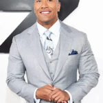 A portrait of actor Dwayne Johnson smiling warmly in a patterned suit jacket.