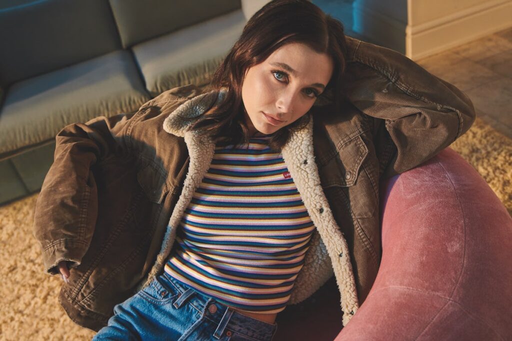 A high-fashion, minimalist portrait of internet personality Emma Chamberlain, styled in chic retro-inspired clothing with her signature deadpan, artistic gaze.