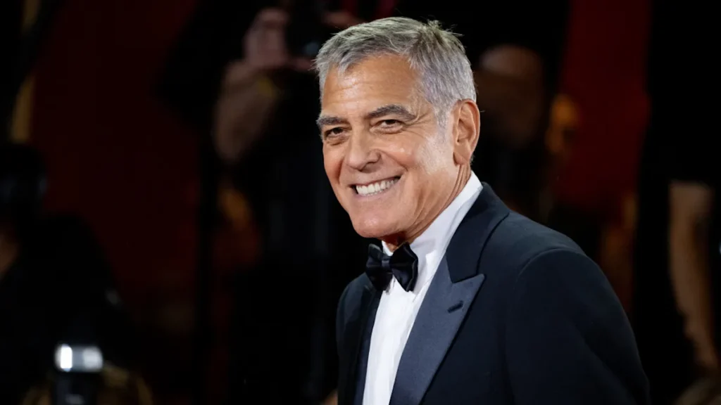 A sophisticated, close-up headshot of actor George Clooney, showcasing his classic silver hair, warm smile, and a formal tuxedo.
