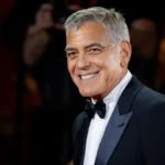A sophisticated, close-up headshot of actor George Clooney, showcasing his classic silver hair, warm smile, and a formal tuxedo.