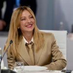 A professional headshot of Italian Prime Minister Giorgia Meloni, smiling professionally at a press conference.