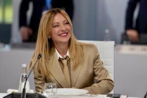 A professional headshot of Italian Prime Minister Giorgia Meloni, smiling professionally at a press conference.