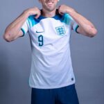 A professional sports portrait of football player Harry Kane in his team uniform, looking forward with a determined smile.