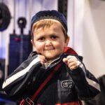 A charming portrait of internet personality Hasbulla Magomedov, smiling and raising a fist in his signature playful pose.