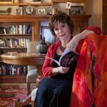 A professional photo of Chilean-American author Isabel Allende, sitting elegantly against a soft-focus library background.