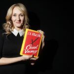 A portrait of author Joanne Rowling smiling and holding up a copy of her new book at a book launch event