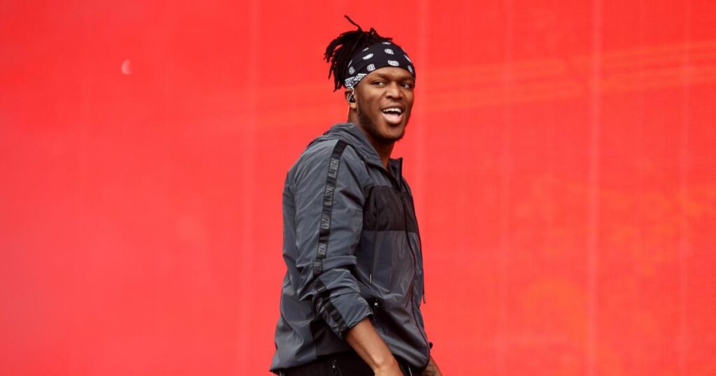 A charismatic portrait of YouTuber and boxer KSI, wearing his signature bandana and styled athletic wear, smiling at the camera.