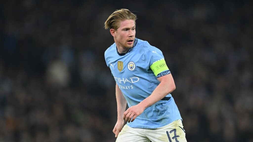 An action shot of midfielder Kevin De Bruyne mid-match, intently looking downfield in his team kit.