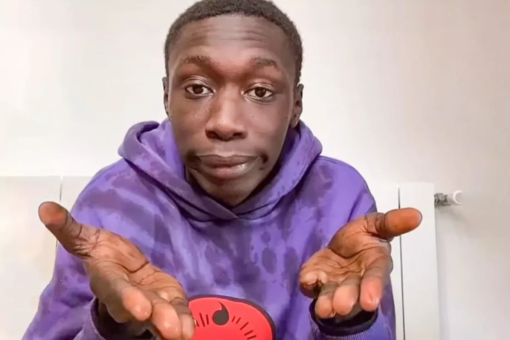 A playful portrait of content creator Khaby Lame, making his famous hand-shrugging gesture with an expressive, deadpan facial expression.