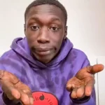 A playful portrait of content creator Khaby Lame, making his famous hand-shrugging gesture with an expressive, deadpan facial expression.