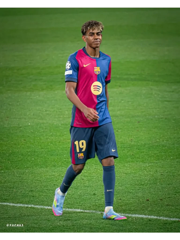 A candid action shot of professional footballer Lamine Yamal on the pitch, wearing his team kit and looking focused.
