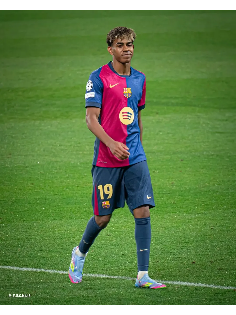 A candid action shot of professional footballer Lamine Yamal on the pitch, wearing his team kit and looking focused.