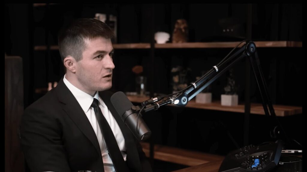 Lex Fridman wearing a suit and tie, speaking over the microphone.