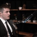 Lex Fridman wearing a suit and tie, speaking over the microphone.