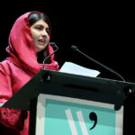 Activist Malala Yousafzai addressing an audience from a podium at a global event.