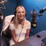 Actress Margot Robbie smiling and speaking during a film panel discussion.