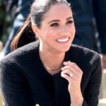 A beautiful, professional headshot of Meghan, Duchess of Sussex, smiling warmly with her hair pulled back, wearing clean, minimalist attire.