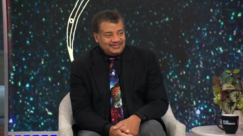 Astrophysicist Neil deGrasse Tyson sitting elegantly and smiling warmly.