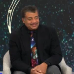 Astrophysicist Neil deGrasse Tyson sitting elegantly and smiling warmly.