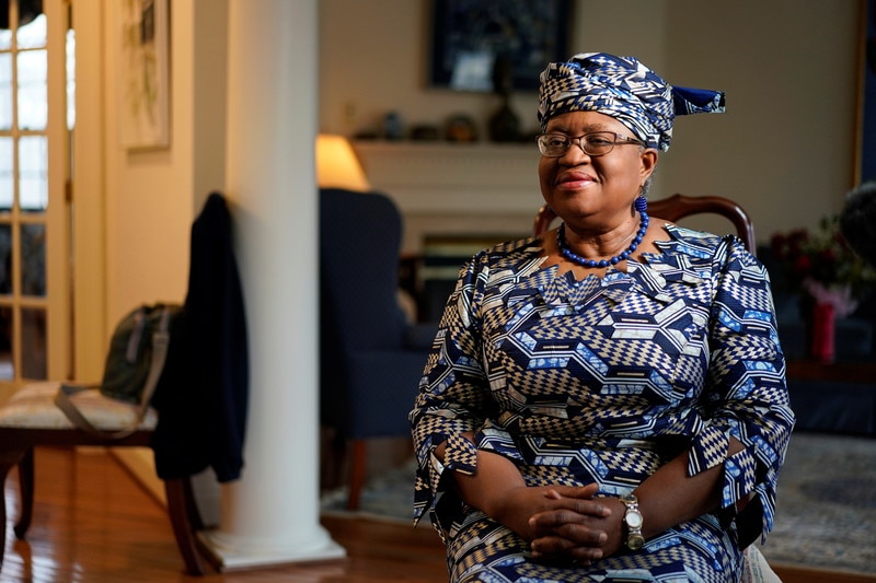 A close-up portrait of WTO Director-General Dr. Ngozi Okonjo-Iweala, smiling warmly in her signature vibrant Ankara print dress and traditional headtie (gele).
