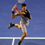 An intense action shot of tennis player Novak Djokovic executing a powerful backhand on a hard court.