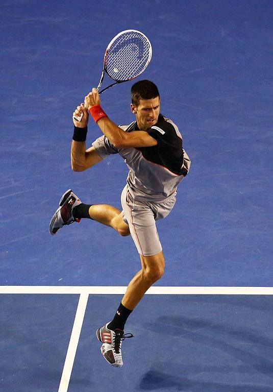An intense action shot of tennis player Novak Djokovic executing a powerful backhand on a hard court.