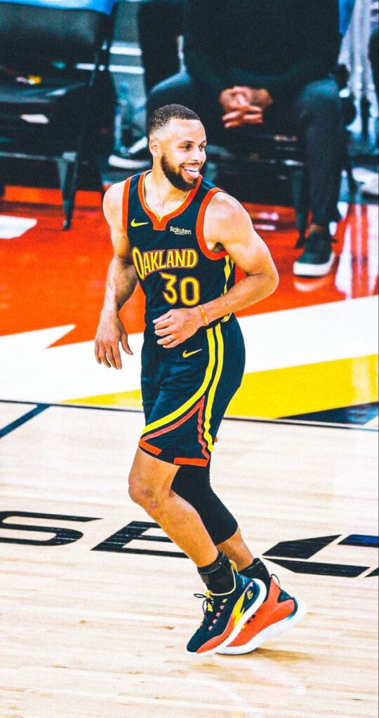 A candid shot of NBA player Stephen Curry smiling broadly on the basketball court during a game.