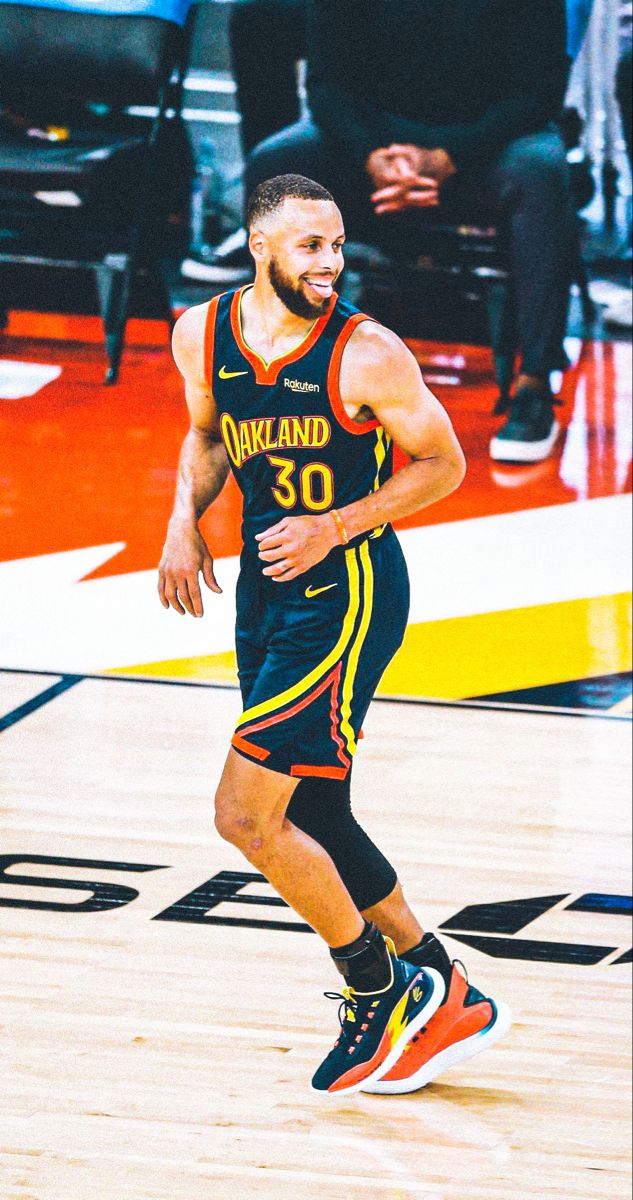 A candid shot of NBA player Stephen Curry smiling broadly on the basketball court during a game.