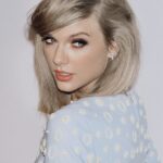 Taylor Swift posing for a portrait in a light-colored outfit.
