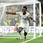 A dynamic photo of Vinícius Júnior celebrating a goal on the football field in his team jersey.