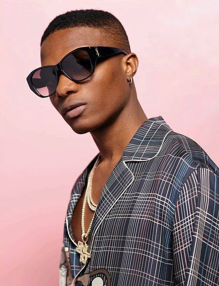 A stylish, high-fashion portrait of Nigerian musician Wizkid, wearing designer sunglasses and trendy minimalist apparel.