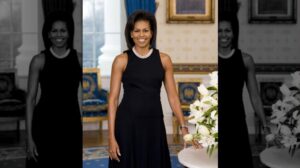 A warm, professional portrait of former First Lady Michelle Obama, smiling brightly in a sleeveless dress in her official white house.