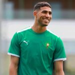 Moroccan professional footballer Achraf Hakimi in a football kit and smiling warmly.