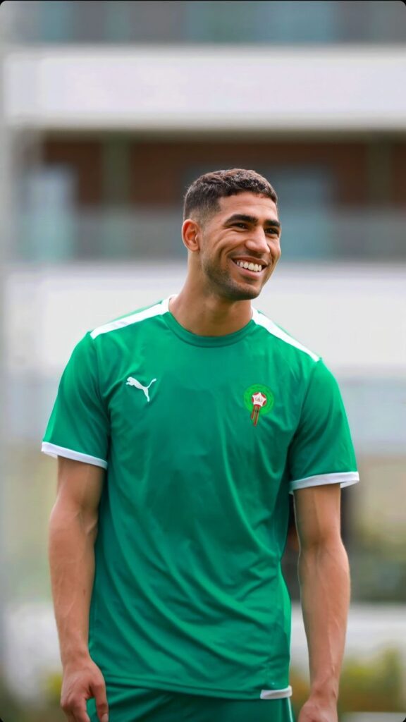 Moroccan professional footballer Achraf Hakimi in a football kit and smiling warmly.