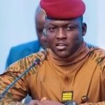 Official portrait of Ibrahim Traoré, President of Burkina Faso, wearing military camouflage uniform and red beret, speaking at a podium.