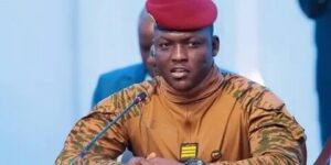 Official portrait of Ibrahim Traoré, President of Burkina Faso, wearing military camouflage uniform and red beret, speaking at a podium.